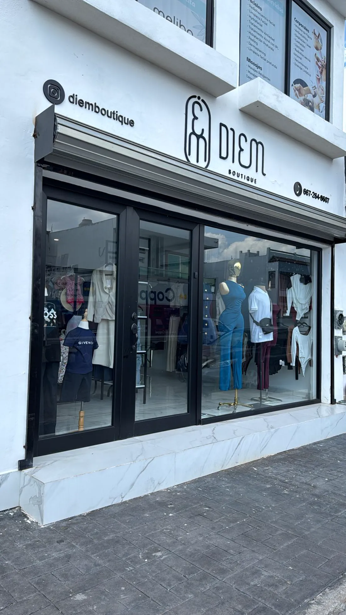 Fachada de DIEM Boutique: muro blanco, cancelería negra, zoclo de mármol blanco y el rótulo DIEM Boutique sobre la entrada.