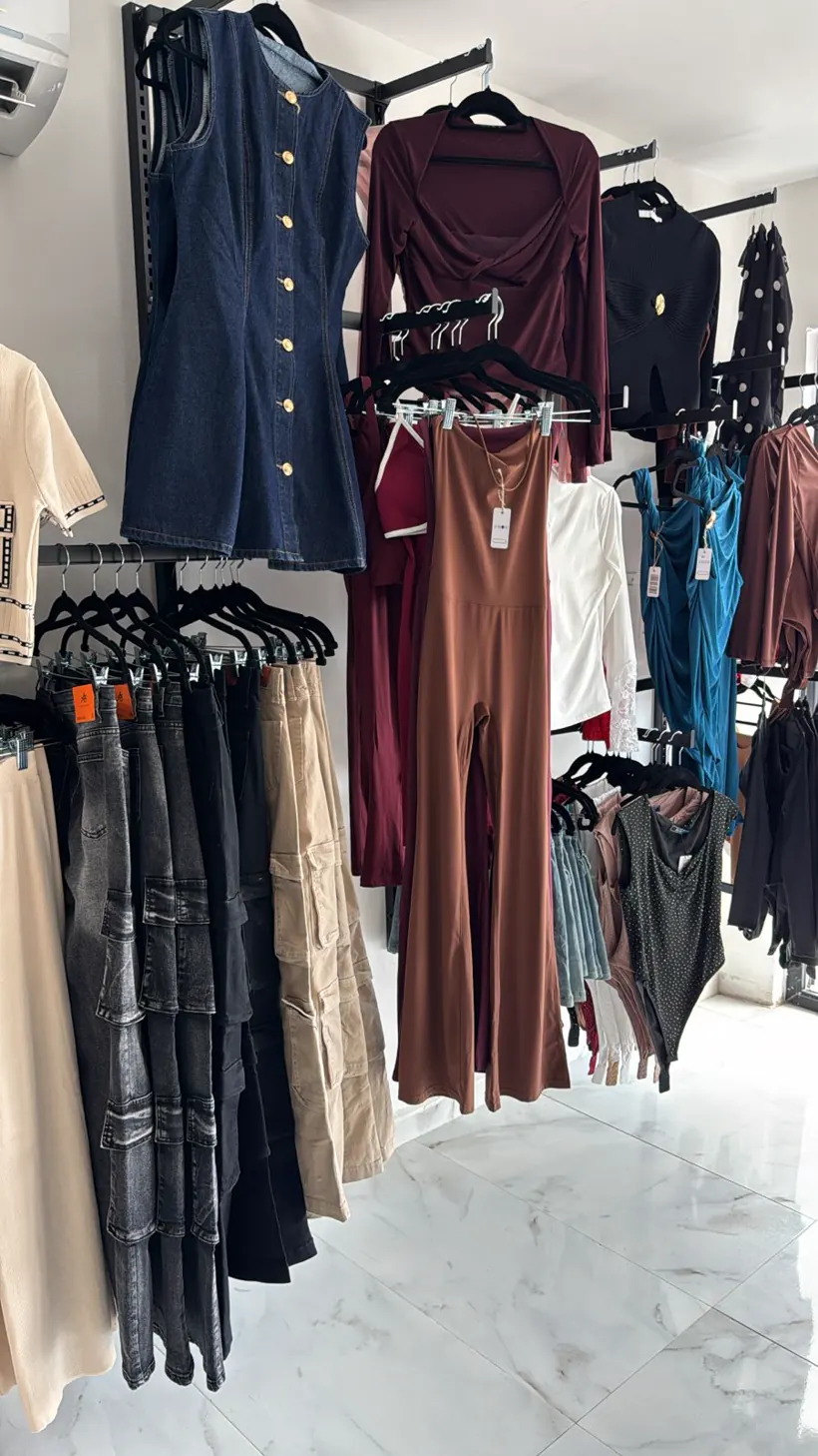 Interior: rieles negros con vestidos, pantalones y prendas de mujer sobre piso de mármol blanco.