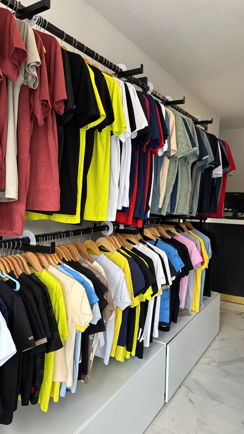 Interior: dos rieles negros con playeras y polos de hombre sobre una base blanca.